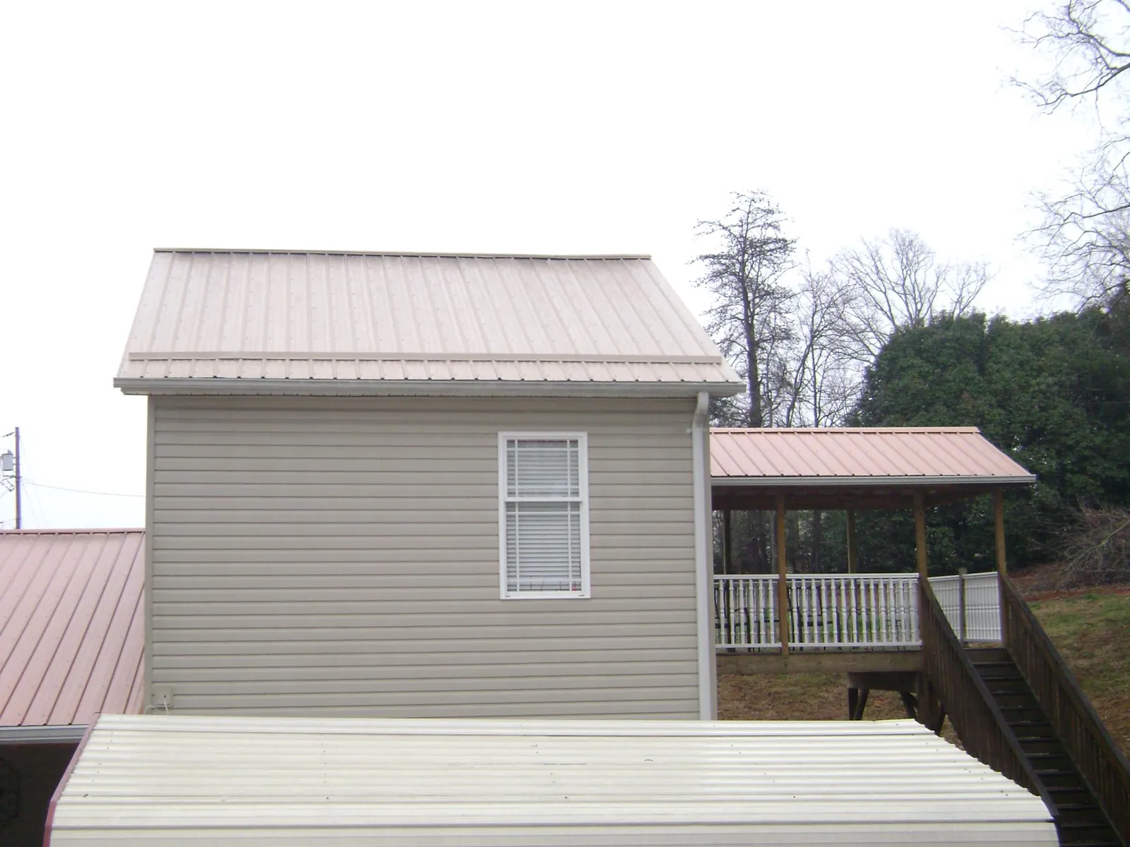 Tan metal roofs on a two story addition and attached porch, from a Roof Replacement job in Andalusia